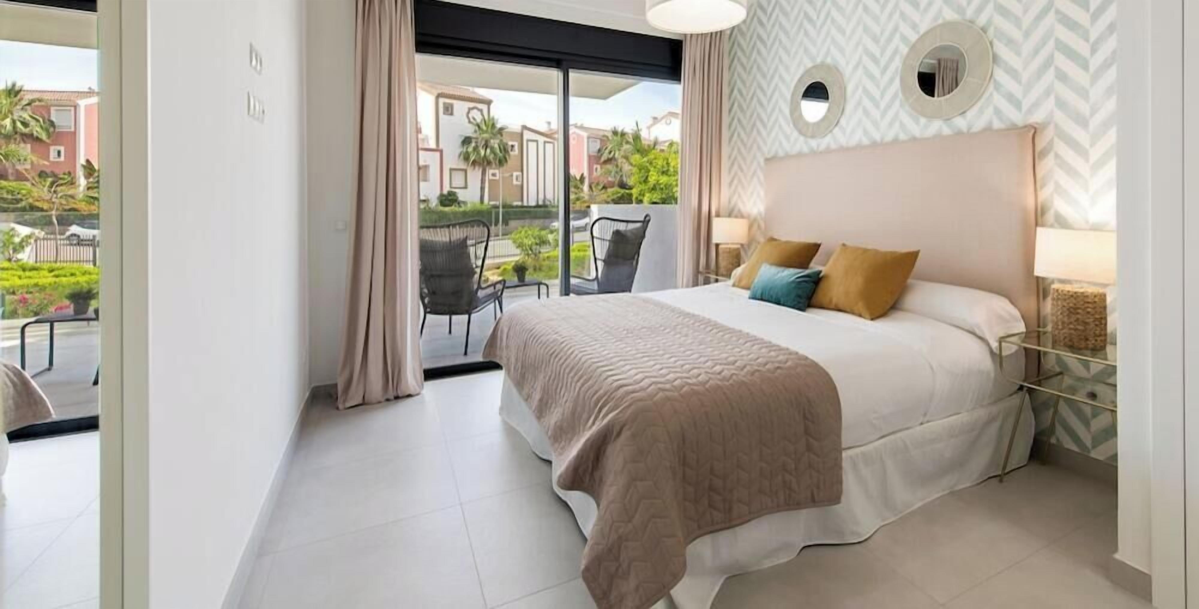 Un dormitorio con cama, ventana, una silla y vistas a edificios y follaje.