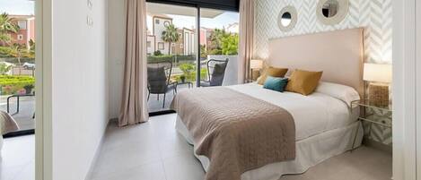 Un dormitorio con cama, ventana, una silla y vistas a edificios y follaje.