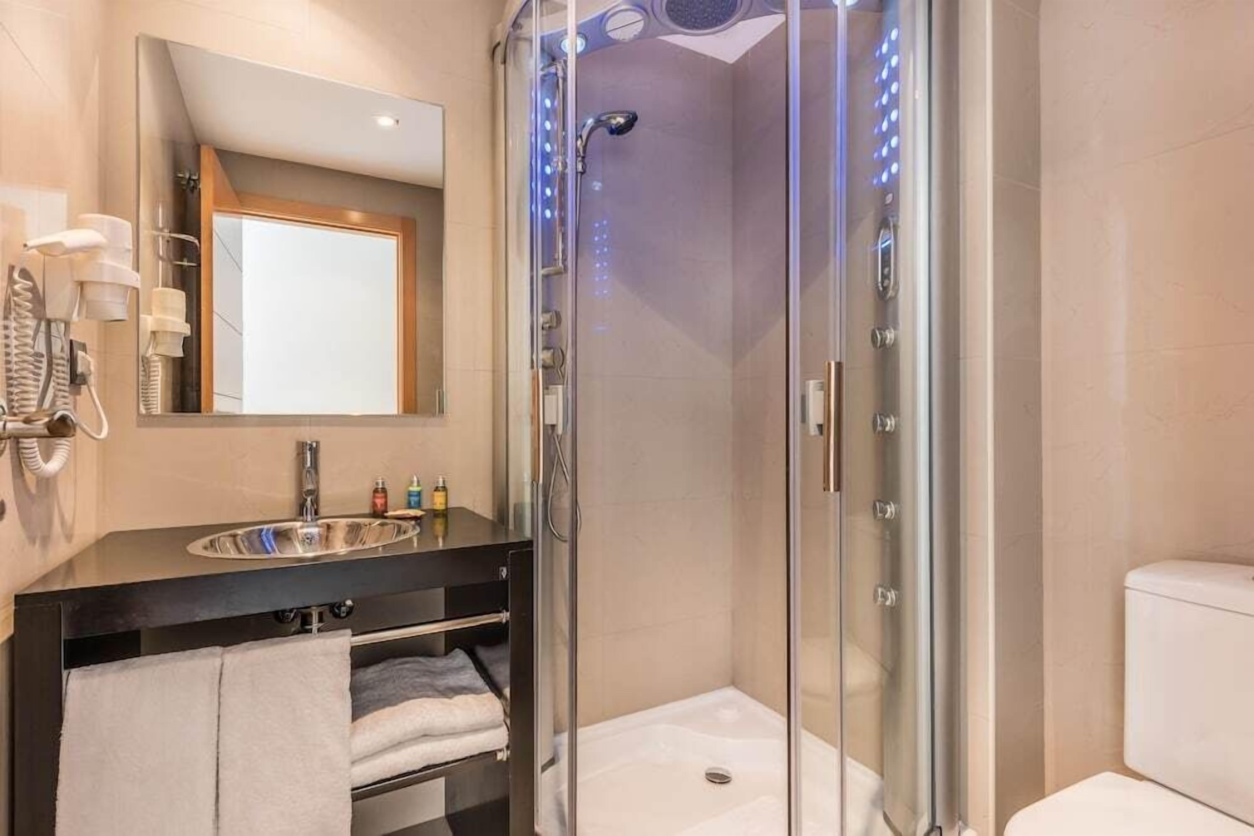 A modern bathroom with a glass-enclosed shower, a sink with a mirror above, and a toilet.