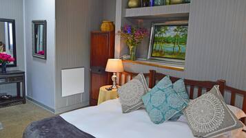 Una habitación de hotel ordenada con cama, mesita de noche con lámpara, espejo, cómoda y estante con adornos.