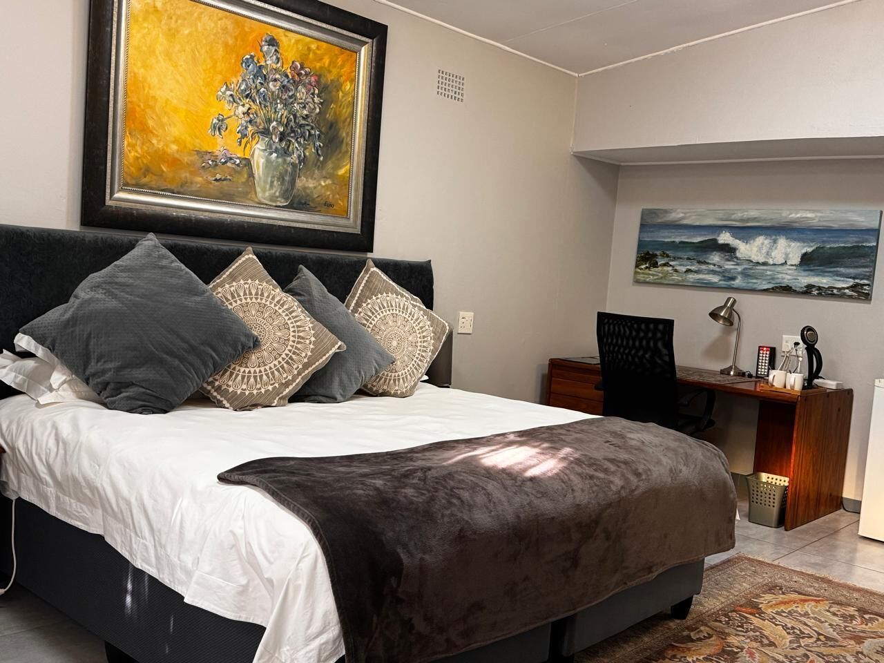 Quarto com cama, escrivaninha e duas pinturas na parede.