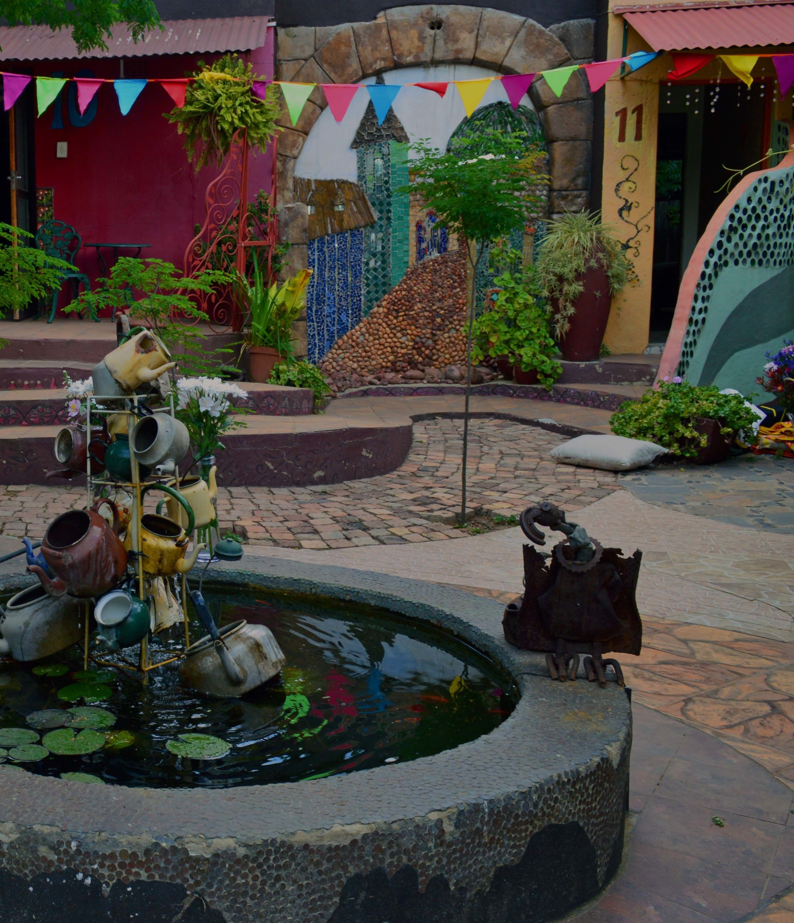 Un patio con una fuente, plantas en macetas y una escultura decorativa de metal.