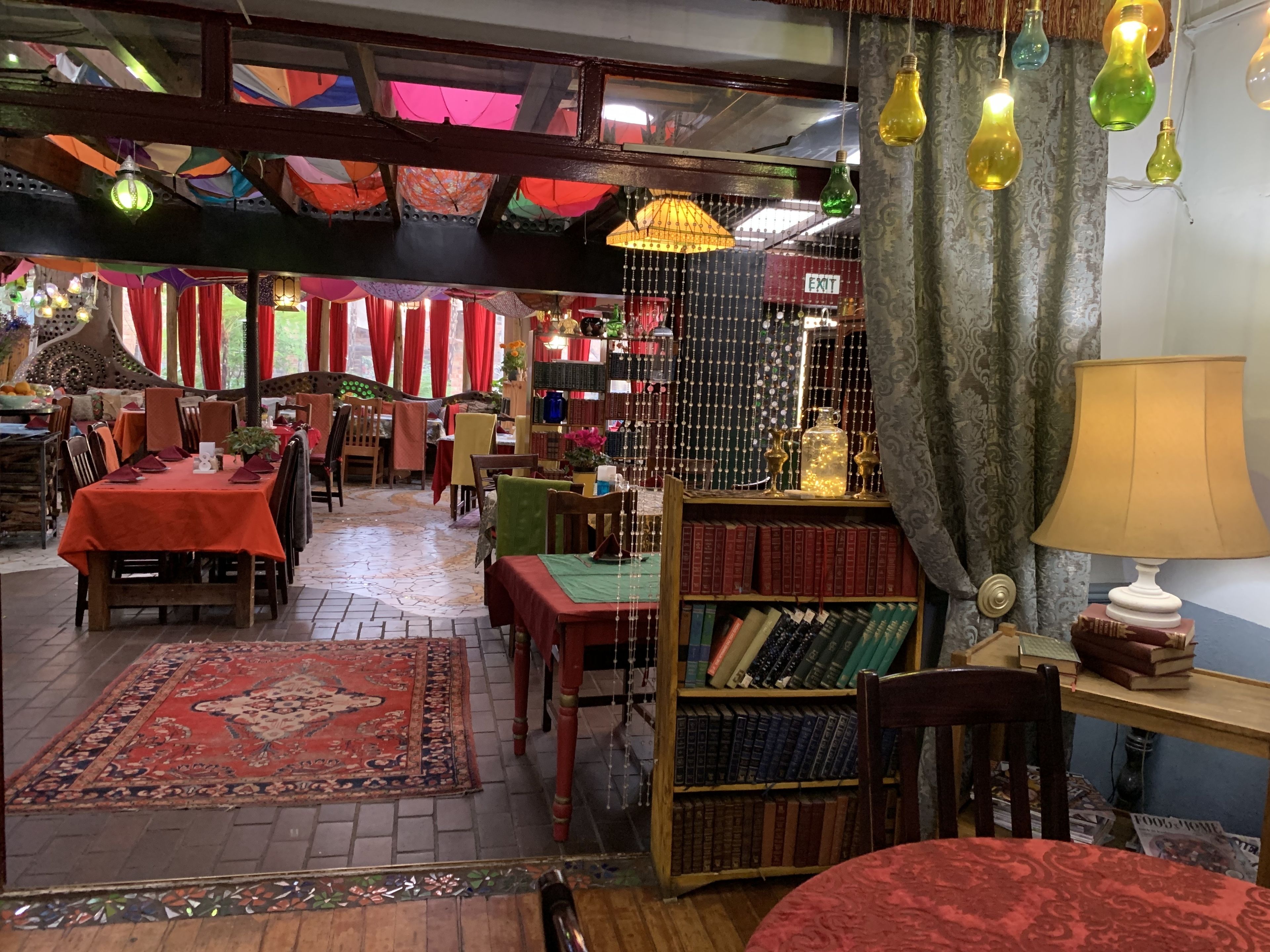 Un restaurant chaleureux avec des tables en bois, des nappes rouges et différents types de luminaires suspendus.