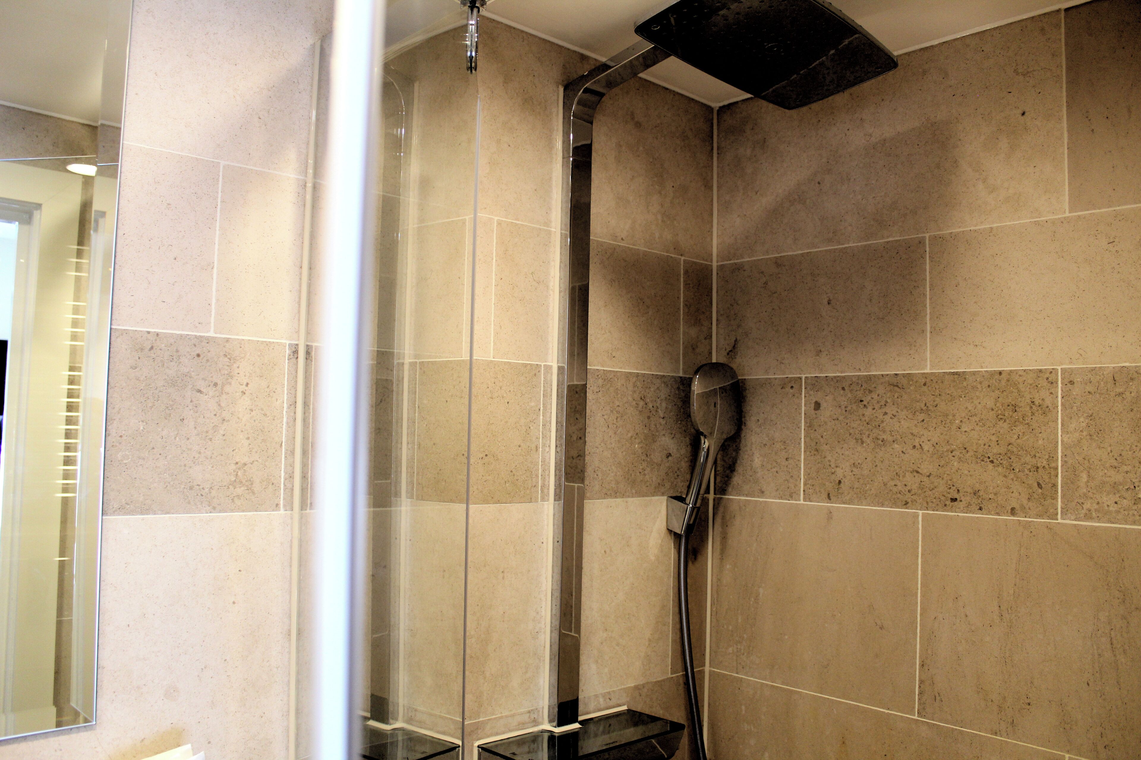 Une douche avec une porte en verre, des murs carrelés et un pommeau de douche amovible.
