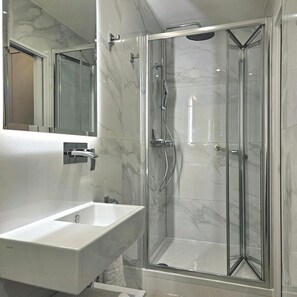 A modern bathroom with a glass-enclosed shower, a white sink, and a large mirror. - 25 Paddington Hotel (London)