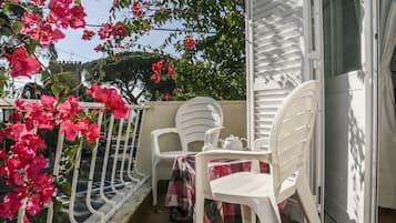 Uma varanda com cadeiras de plástico branco e uma mesa, coberta por toalha de mesa quadriculada vermelha e preta.
