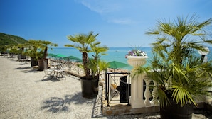 A beachside café with outdoor seating, potted plants, and a view of the sea. - Royal Bay Hotel – All Inclusive (Elenite)