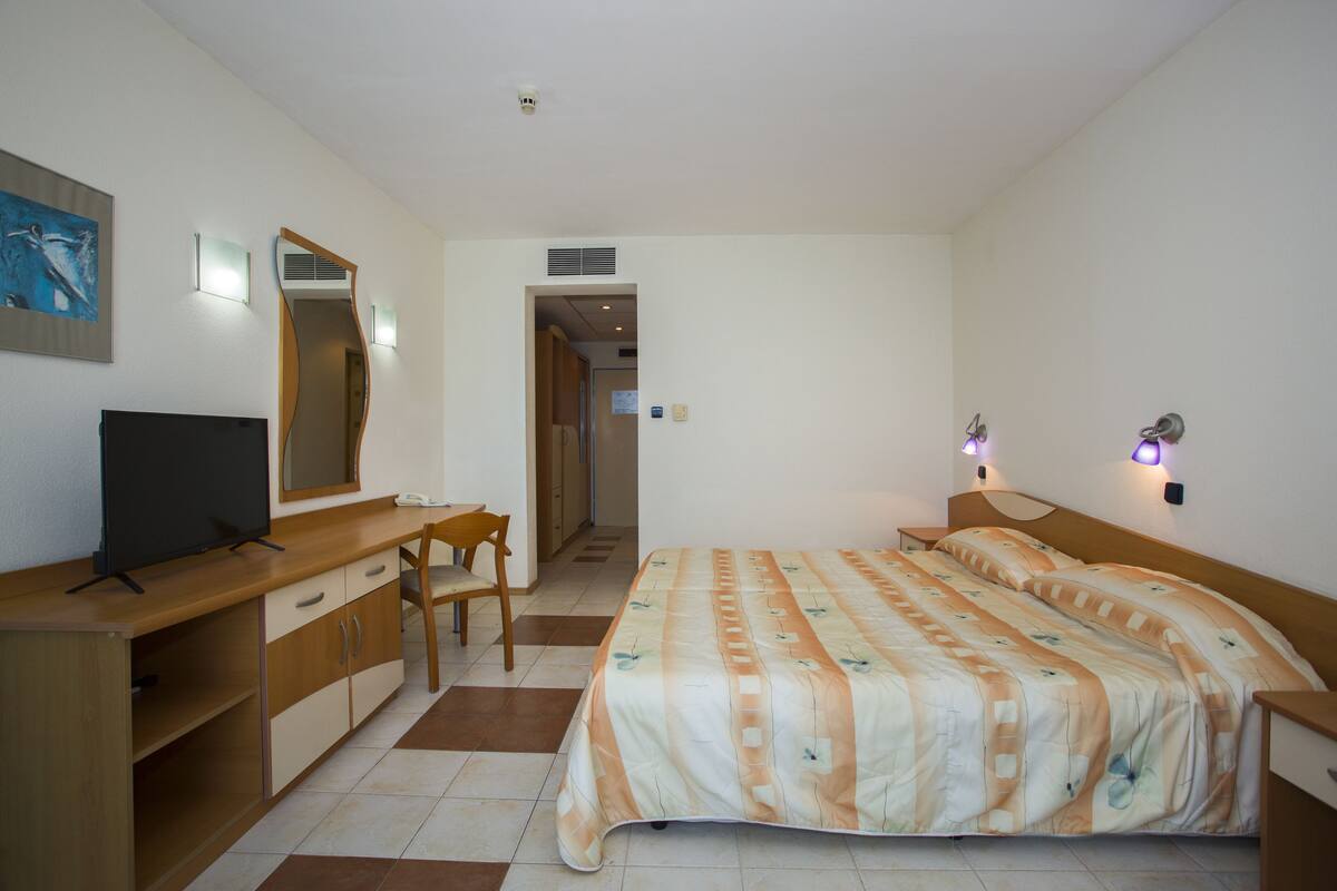 A hotel room with a bed, a desk with a TV, a chair, and a mirror.