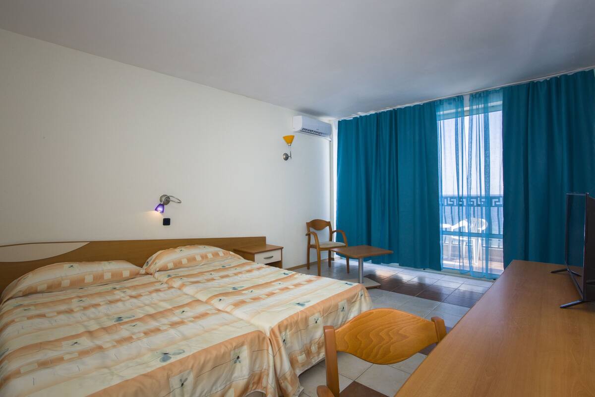A hotel room with a bed, a desk, a chair, and a TV.