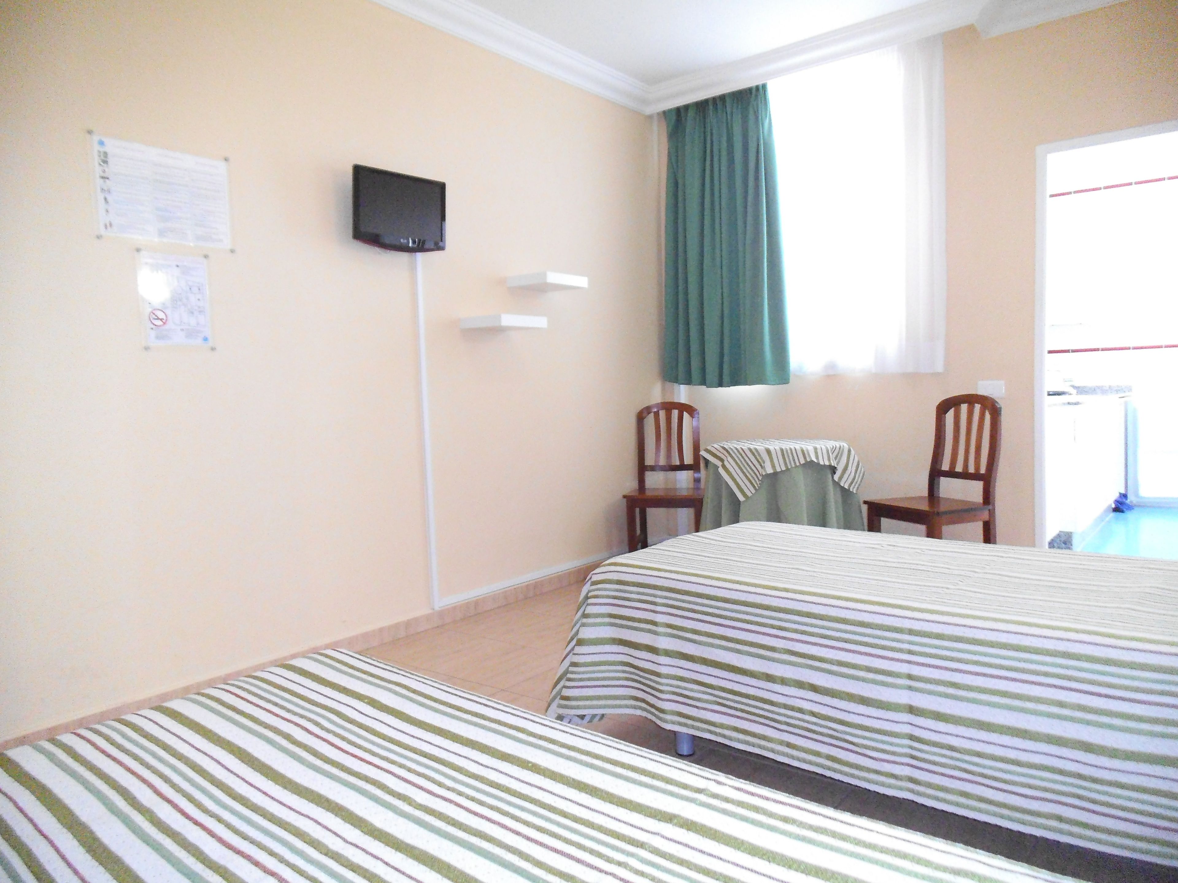 Habitación de hotel con dos camas, un televisor en la pared, una ventana con cortinas y una silla.