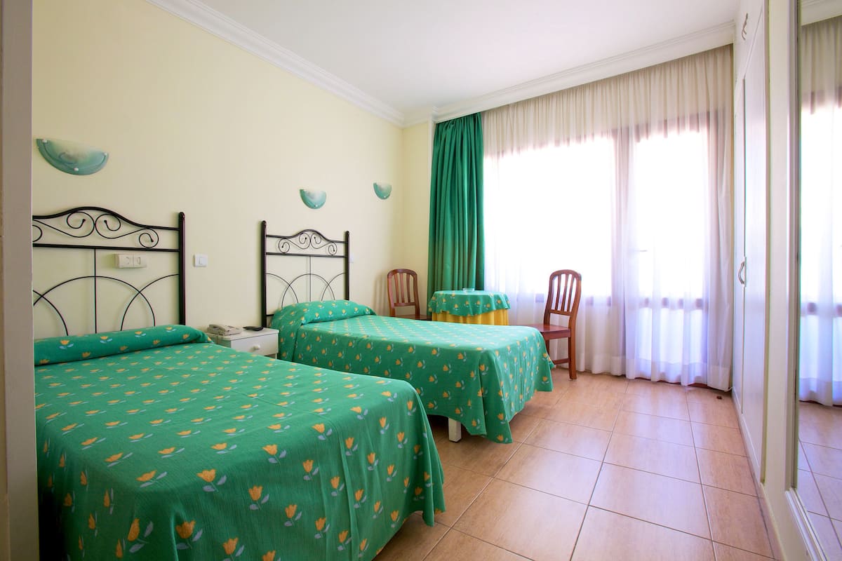 A room with two beds, a chair, a table, and a window with curtains.