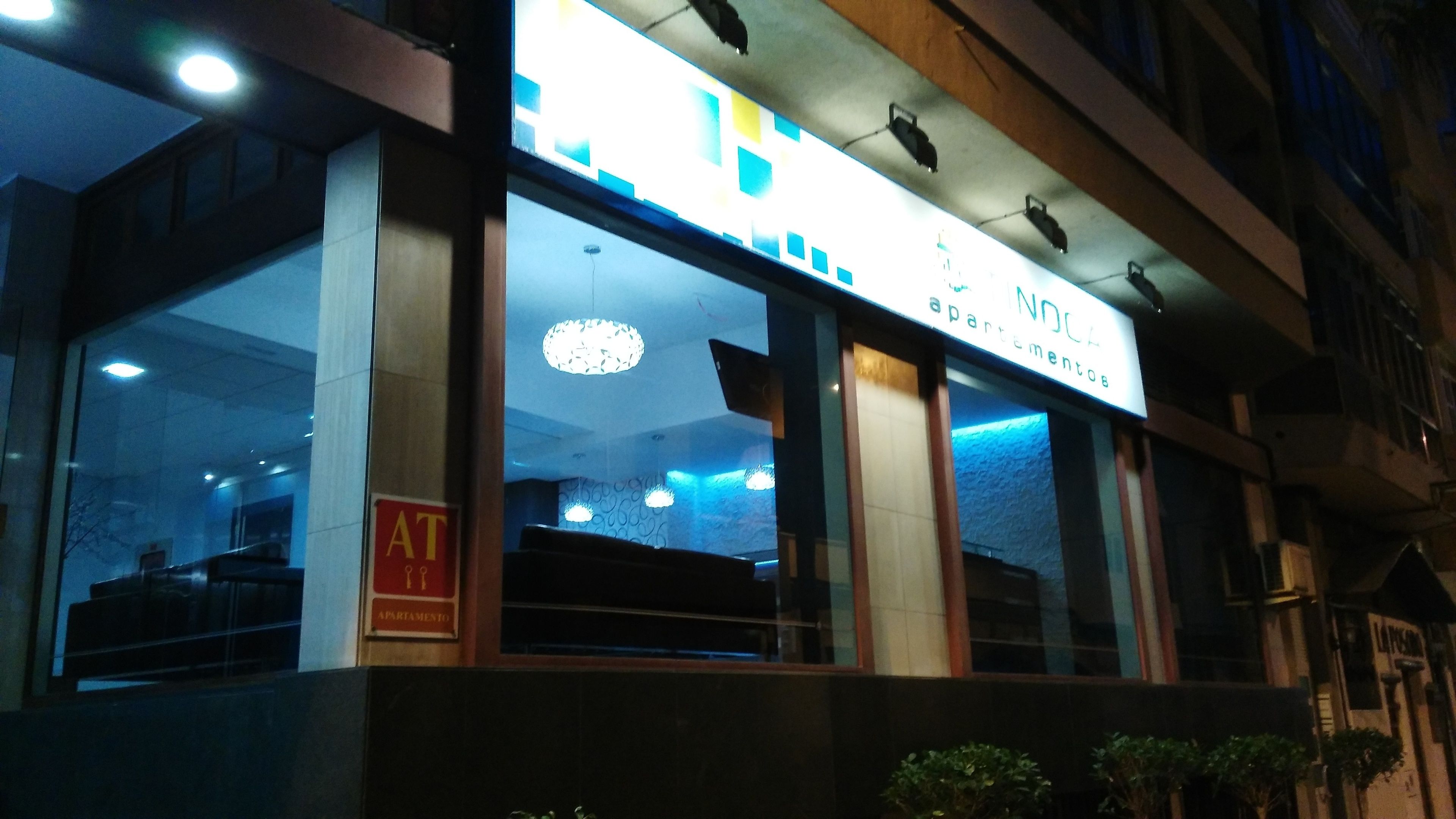 Un edificio con un letrero que dice "NOCA Apartamentos" y una señalización visible de "AT" que indica una entrada o punto de acceso.