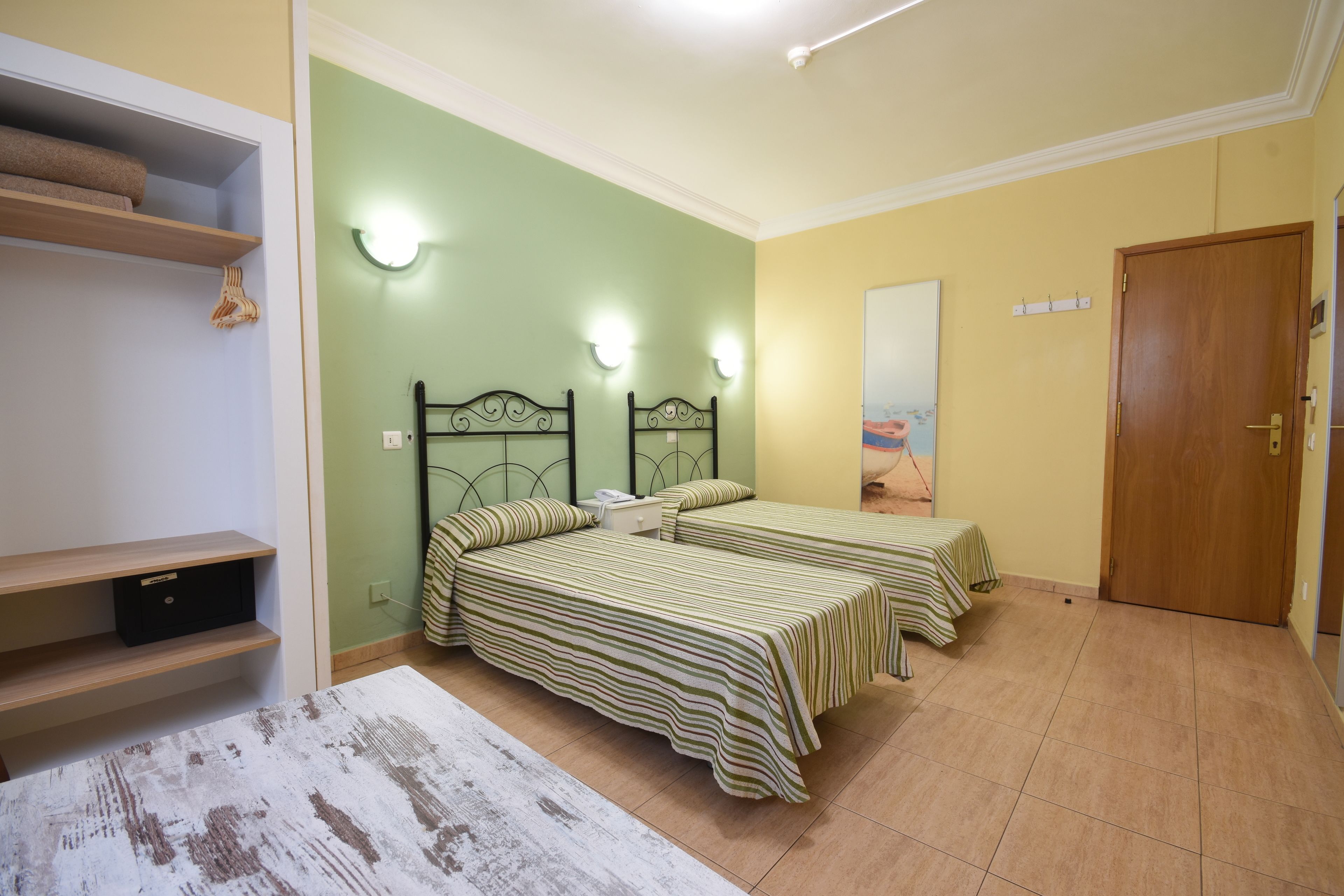 Une pièce avec deux lits, une étagère en bois, un tapis blanc et une porte.