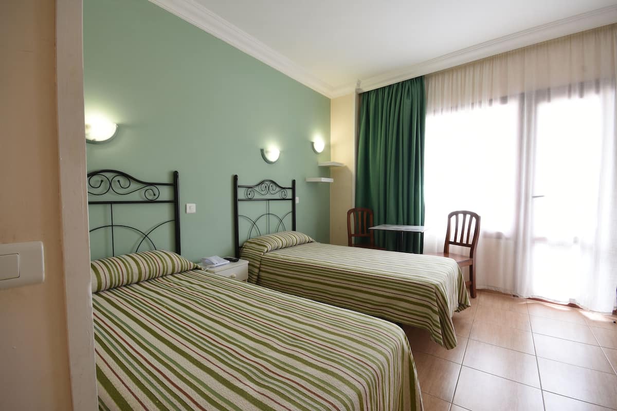 A room with two beds, a chair, a table, and a window with curtains.