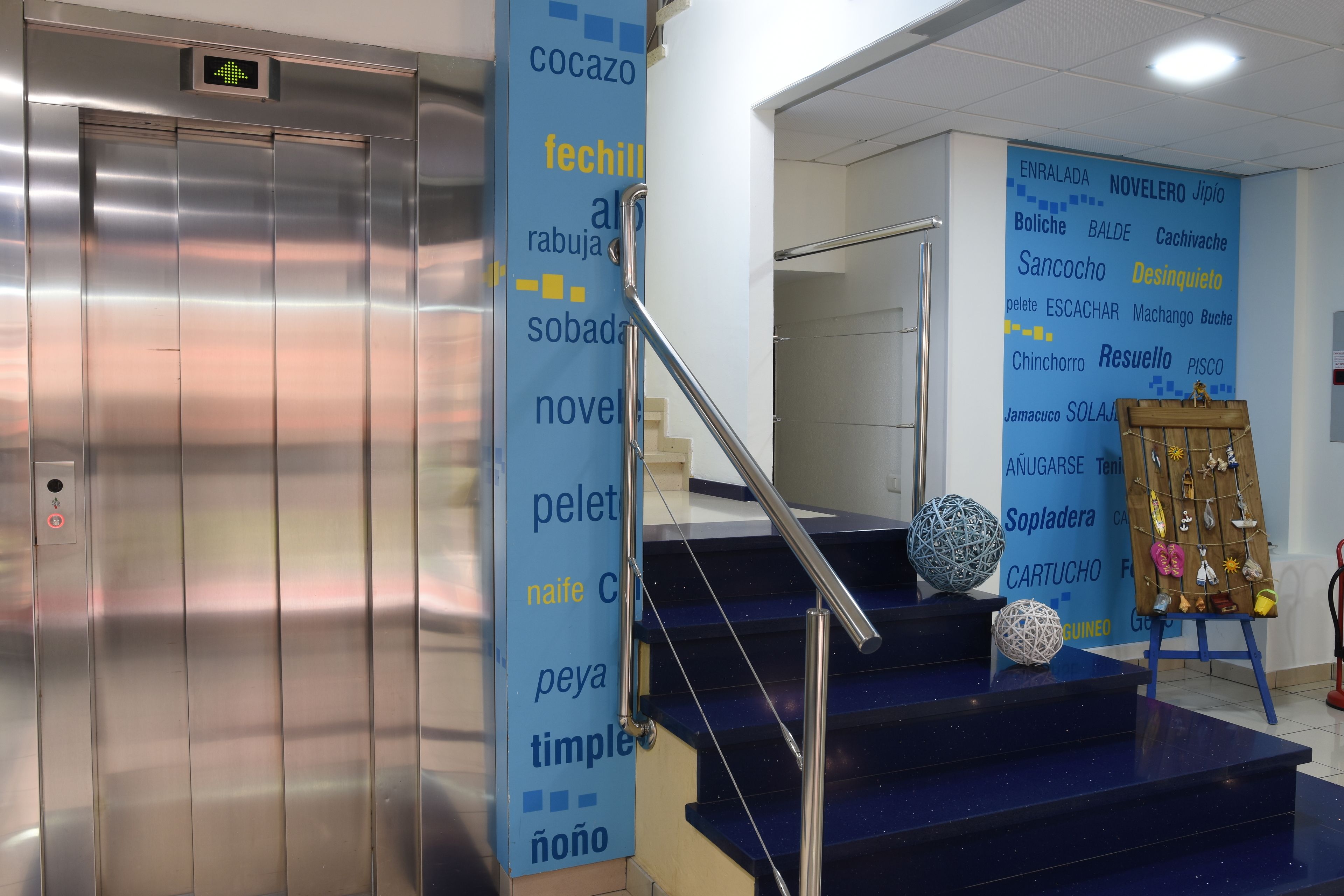 Un ascensor, una escalera con barandilla y una pared con varias palabras en un idioma extranjero.