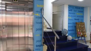 Un ascensor, una escalera con barandilla y una pared con varias palabras en un idioma extranjero.