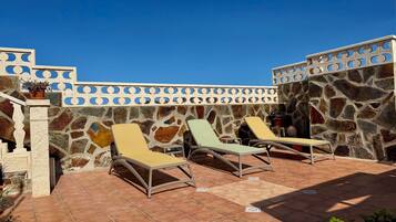 A rooftop terrace with stone walls, two lounge chairs, and a potted plant.