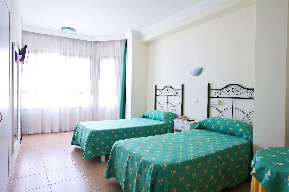 A hotel room with two single beds, a nightstand, a small table, and a window with curtains.