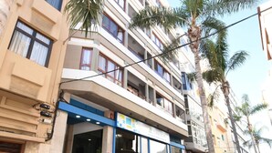 Un hotel de varios pisos con restaurante en la planta baja, palmeras y entrada con adoquines.