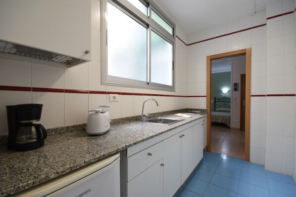 A kitchen with white cabinets, a granite countertop, a coffee maker, and a sink.