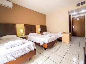 A hotel room with two beds, a bedside table with a lamp, and a door with a sign.