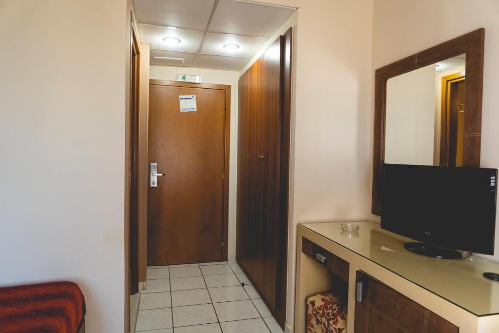 Un pasillo con una puerta de madera, un televisor sobre un mueble de vidrio y un espejo en la pared.