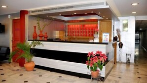 Un comptoir d’accueil aux couleurs rouge et blanc, une plante en pot et un panneau sur le mur.