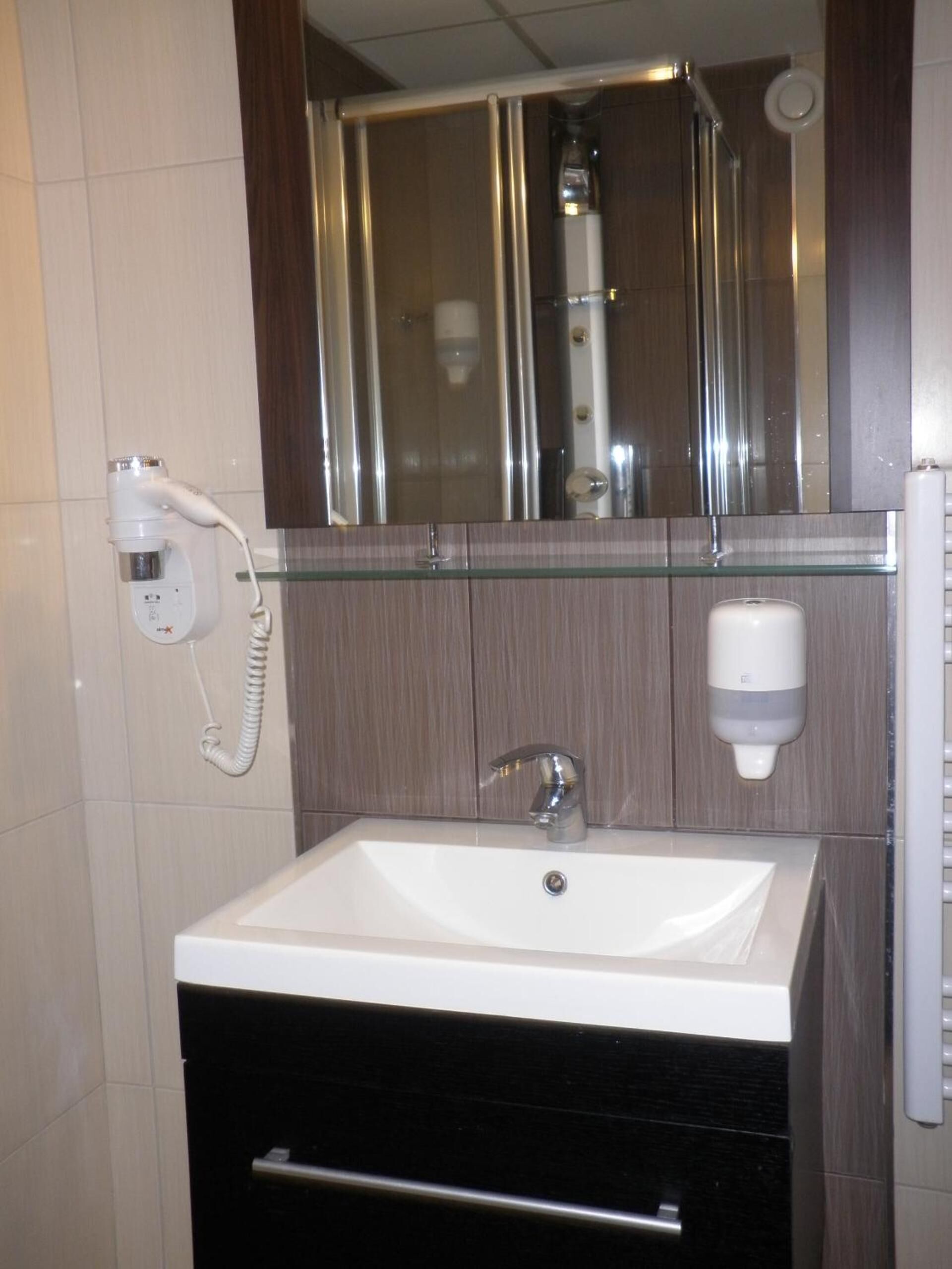 A bathroom with a white sink, a glass shower enclosure, a hand dryer, and a soap dispenser.