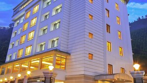 A multi-story hotel with a modern design, featuring a prominent entrance with a glass facade and a well-lit exterior. - Clouds Valley Leisure Hotel (Devikolam)