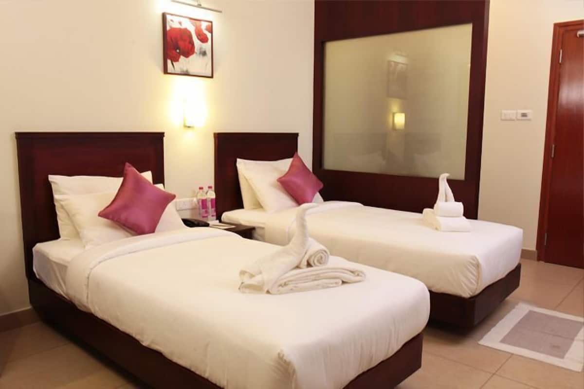 A hotel room with two beds, each with white bedding and a wooden headboard. There is a large mirror on the wall, a painting above the left bed, and a towel on the floor.