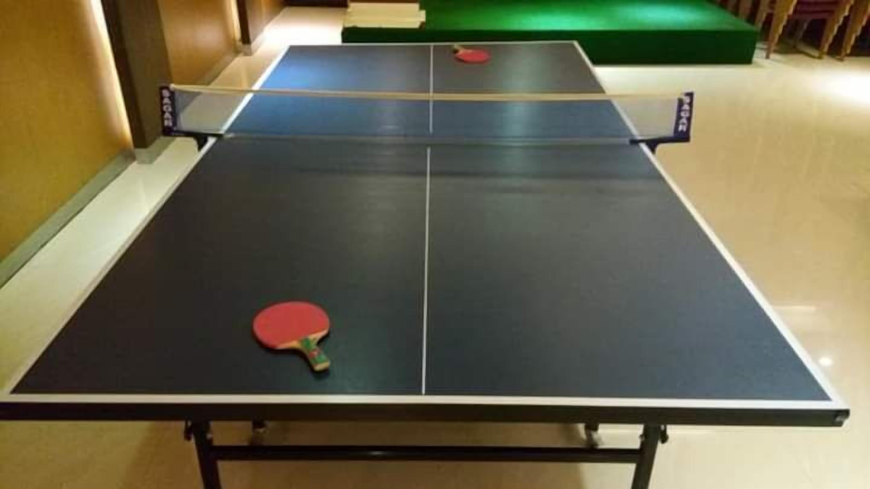 Una mesa de ping pong con una paleta roja en primer plano y otra al fondo.