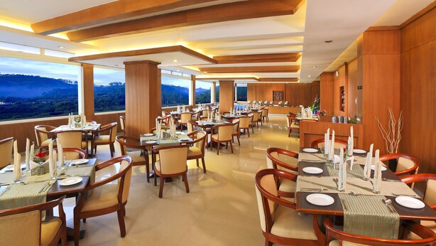 A spacious dining area with multiple tables set for dining, large windows offering scenic views, and wooden paneling on the walls. - Clouds Valley Leisure Hotel (Devikolam)