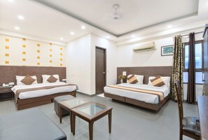 A hotel room with two beds, a small table, a sofa, and a ceiling fan. - Hotel La Vista (New Delhi)