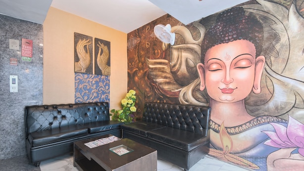 A reception area with a black leather sofa, a wooden coffee table, and a large Buddha mural on the wall. - Hotel La Vista (New Delhi)