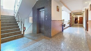 A hotel lobby with a marble staircase, an elevator, and a hallway leading to other rooms. - Hotel La Vista (New Delhi)