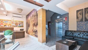 A hotel lobby with a reception desk, a large cityscape mural, a staircase, and a seating area. - Hotel La Vista (New Delhi)