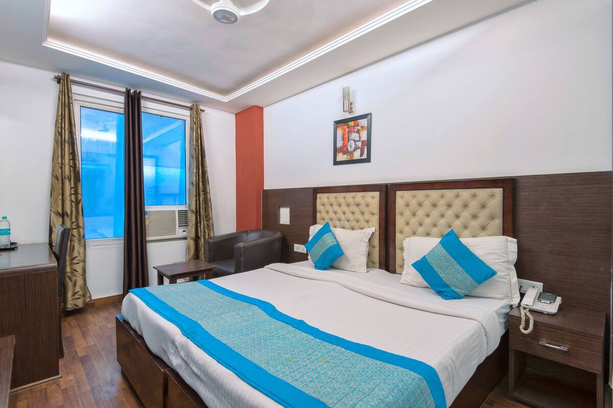 A hotel room with a large bed, a desk, a chair, a bedside table, a phone, and a window with curtains.