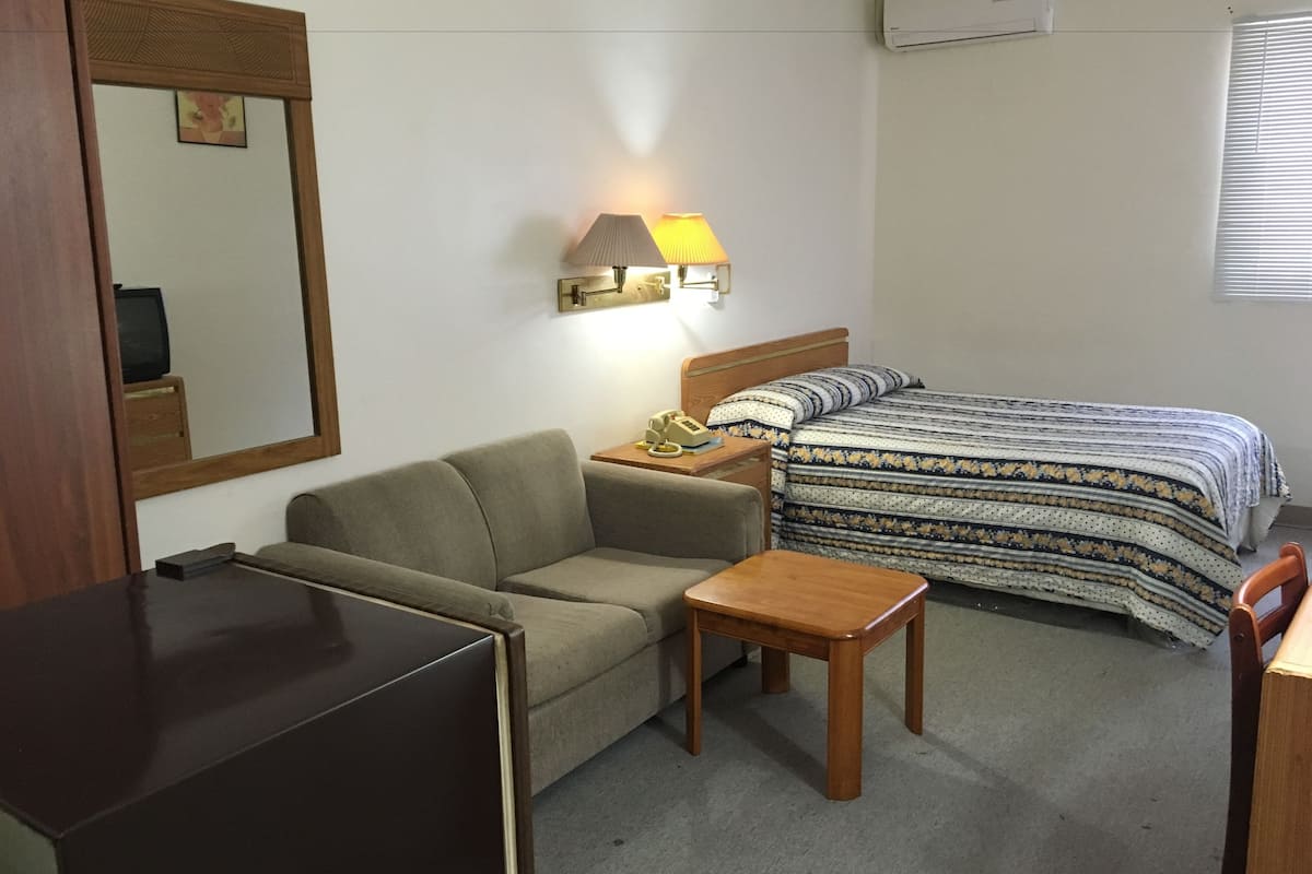 A compact hotel room with a single bed, a sofa, a small table, and a TV.