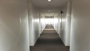 A long, narrow hallway with white walls and a carpeted floor, leading to a door at the end. - Tamuning Plaza Hotel (Tamuning)
