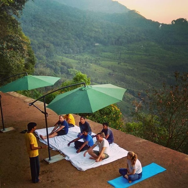 A group of people sitting on mats outdoors with a scenic view of hills in the background. - Blackberry Hills Munnar - Nature Resort & Spa (Devikolam)
