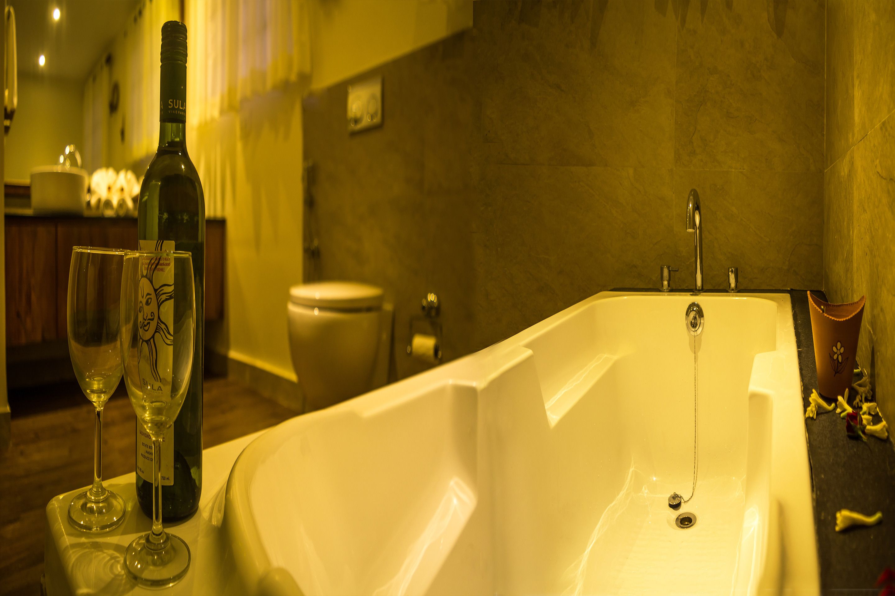 A bathroom with a bathtub, a toilet, and a sink. There is a bottle of wine and two wine glasses on the counter.