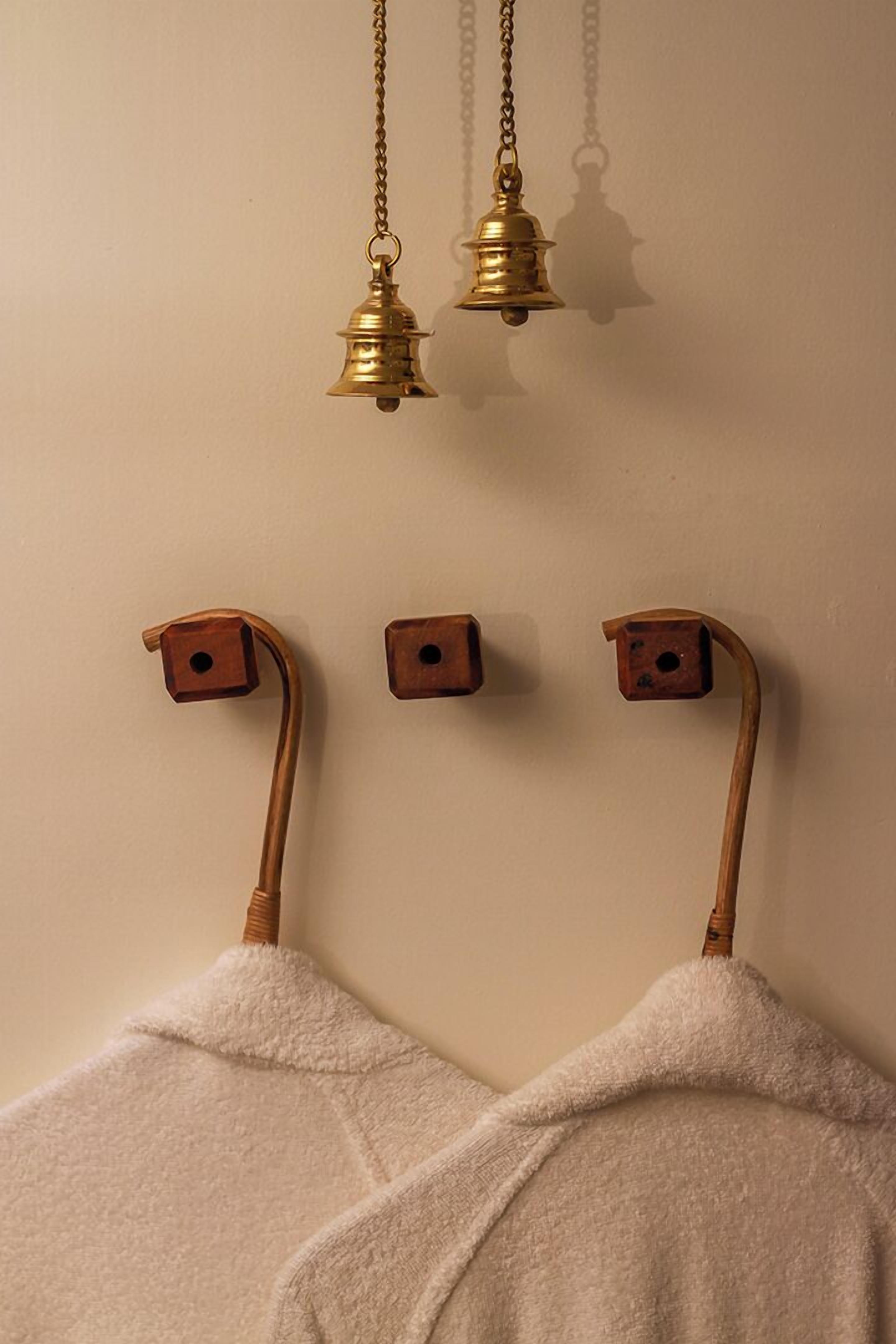 Une salle de bain avec deux porte-serviettes sur lesquels sont disposées des serviettes blanches, une cloche en laiton et un sèche-serviettes en bois.