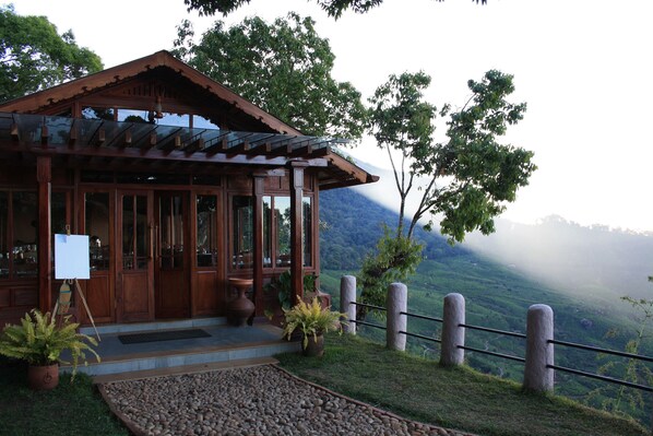 A wooden building with a glass door and windows, surrounded by a stone pathway and potted plants. - Blackberry Hills Munnar - Nature Resort & Spa (Devikolam)