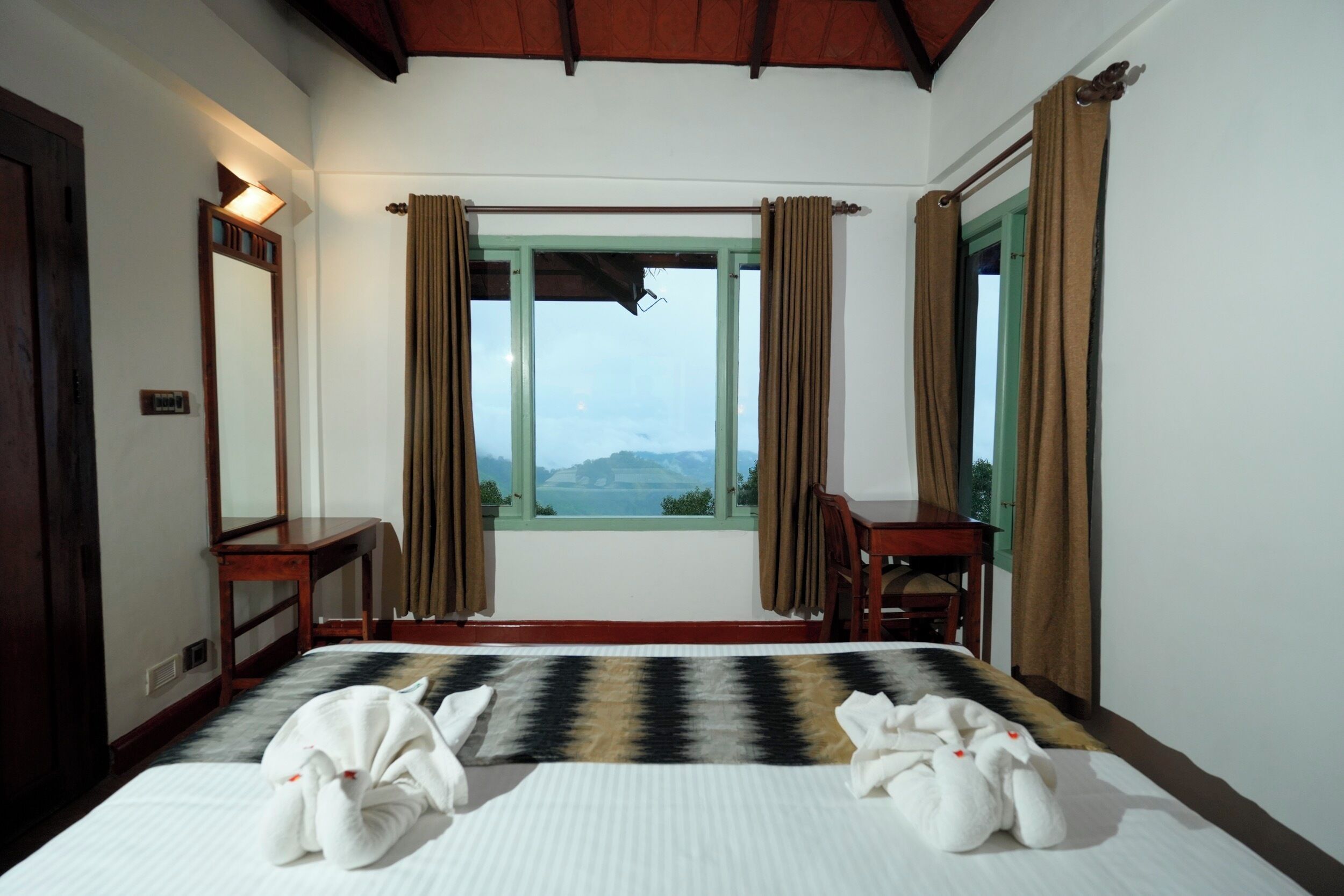 A hotel room with a bed, a desk, a chair, and a window with curtains.