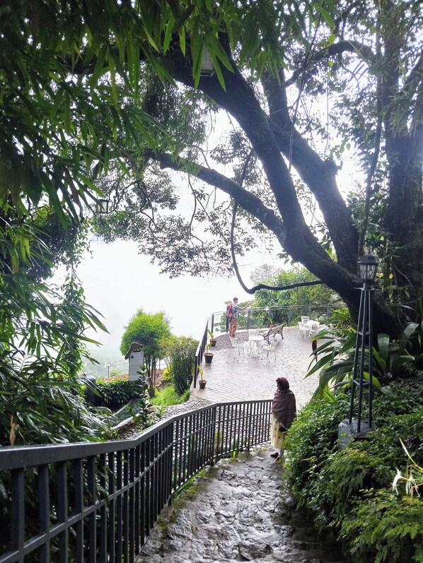 A stone pathway leading up to a seating area with metal railings, surrounded by lush greenery and trees.