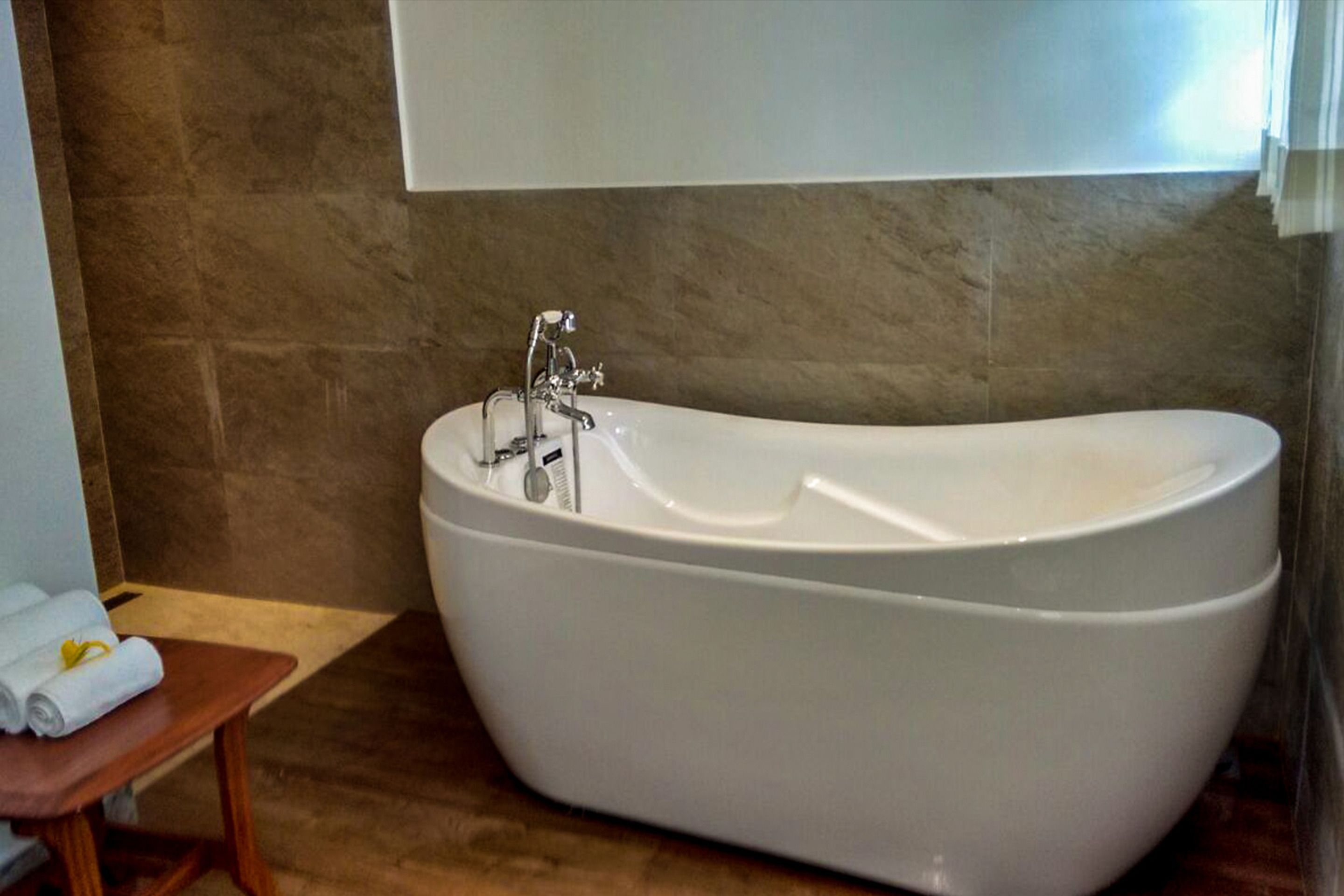 A freestanding bathtub in a bathroom with a wooden bench and towels.