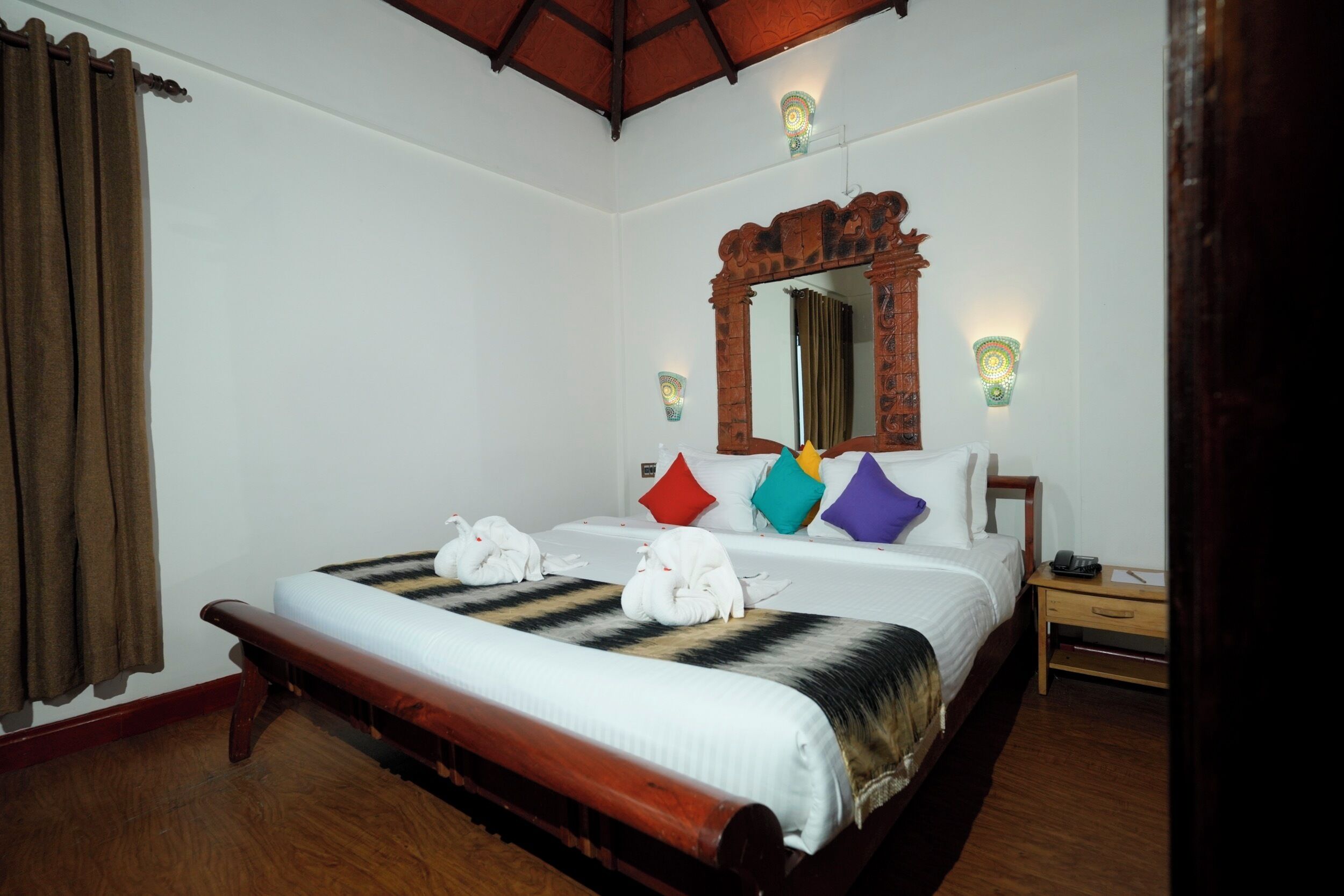 Una habitación de hotel con una cama grande, un banco de madera, un espejo y dos lámparas de noche.