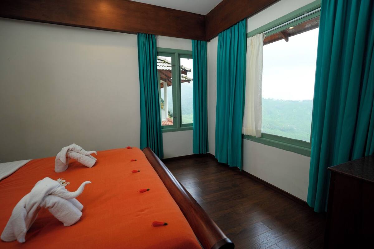 A hotel room with a large bed, teal curtains, and a view of the outdoors.