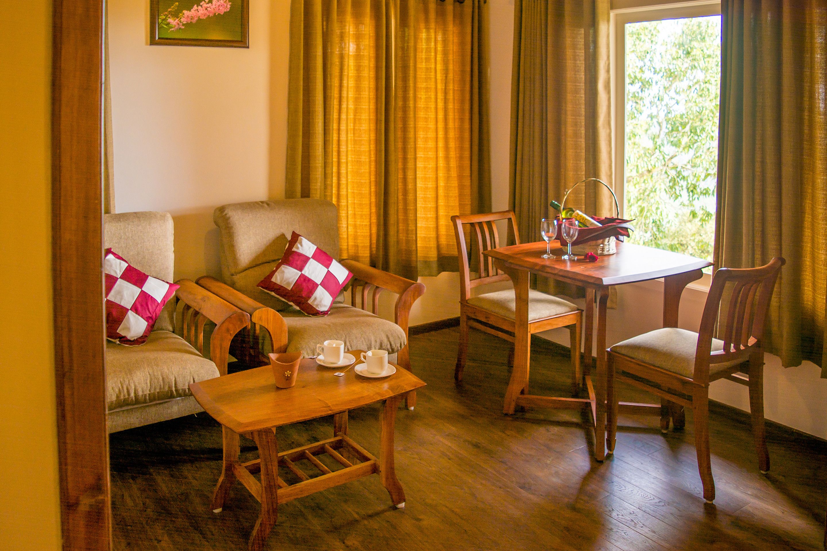 A cozy room with a wooden sofa, a small table, and two chairs. There is a window with curtains, and a painting on the wall.