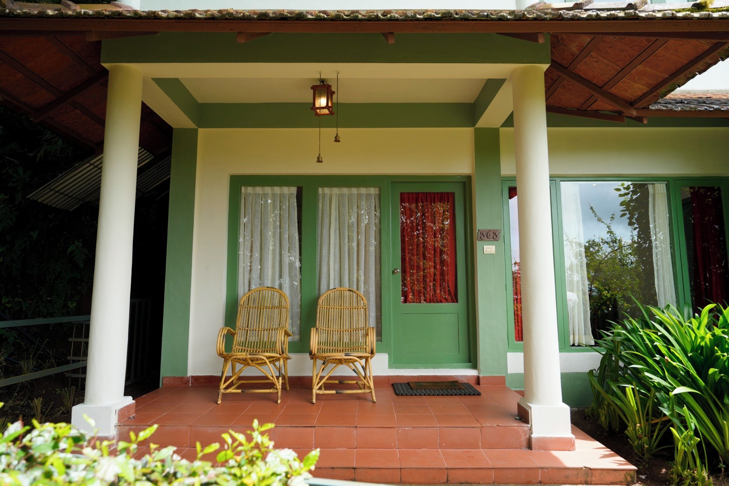 A porch with two wicker chairs, a green door, and a small lantern.